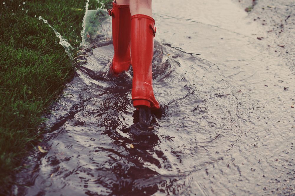 Foto på en flicka med röda stövlar i en vattenpöl
